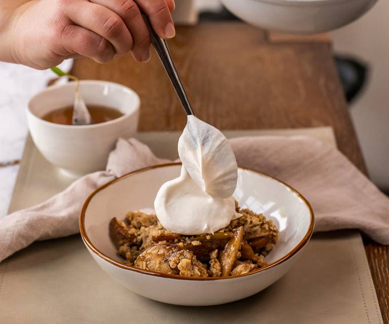 Adding a dollop of whipped cream to a bowl of Bombay Chai Pear Crisp