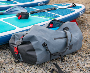 Red Original waterproof kit bag next to paddle board
