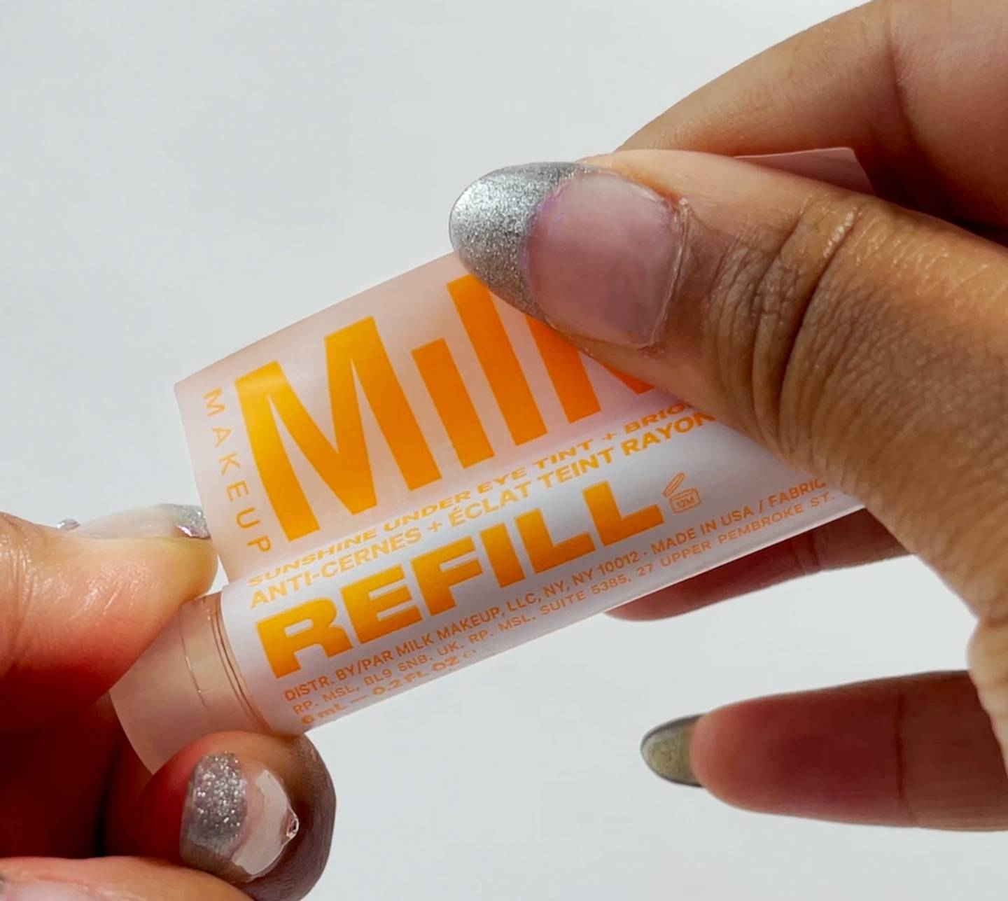 Model holds Milk Makeup Sunshine Under Eye Tint + Brighten Refill Cartridge