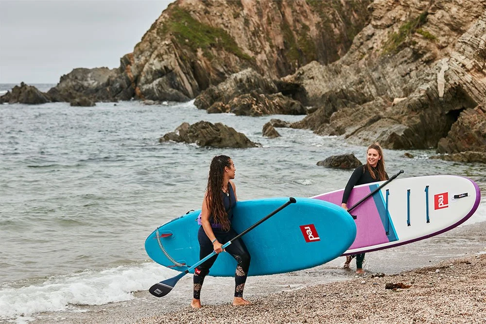 Two women carrying Red Original SUP's out of the sea