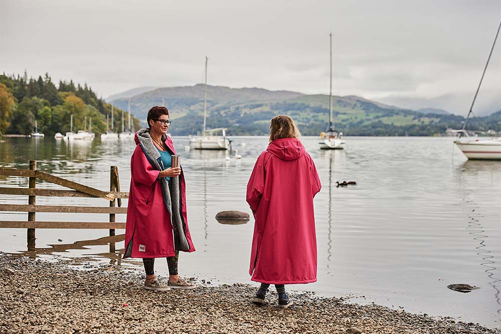 Two women stood by a lake wearing Red Original waterproof changing robes