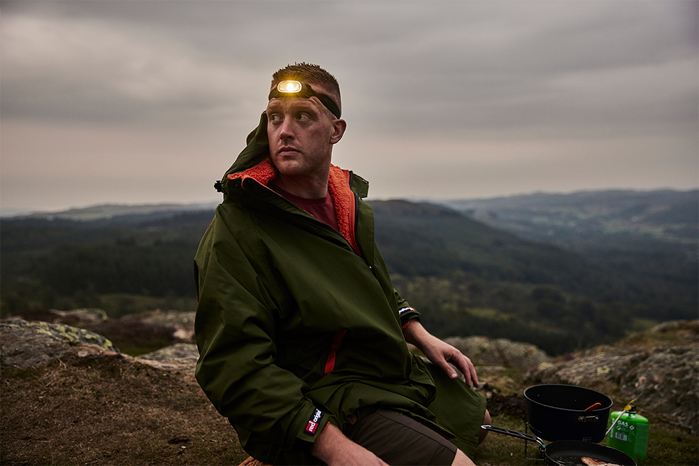 Man wearing head torch sat on rocks in the mountains