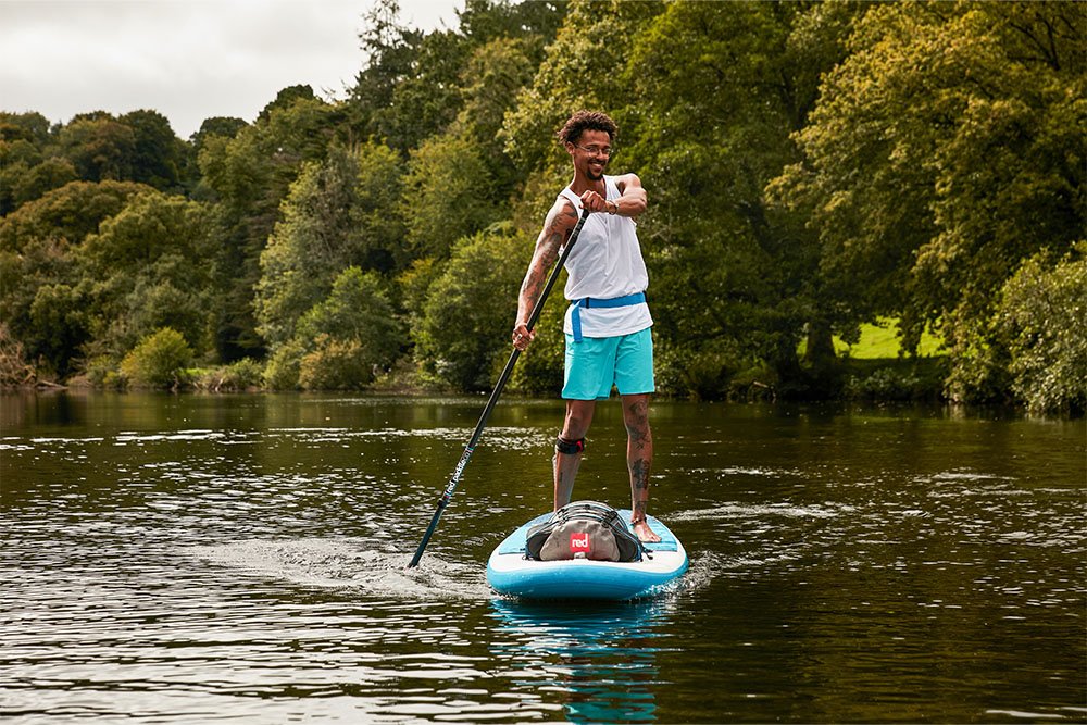 Man paddle boarding with waterproof SUP deck bag attached 
