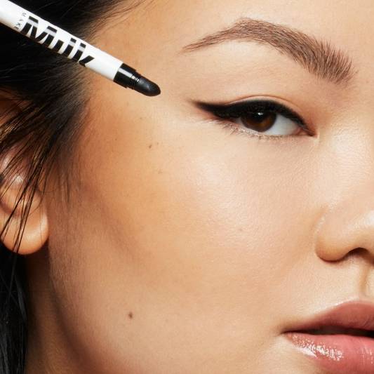 Model wears a cat eye wing drawn with Milk Makeup Infinity Long Wear Eyeliner in Outer Space on a white background. The wing is smudged out.