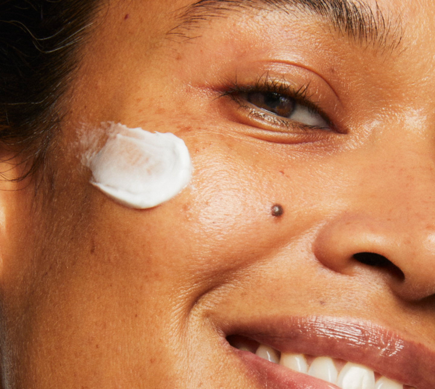 Close-up portrait of a model smiling. They are wearing a swipe of Milk Makeup Vegan Milk Moisturizer on their face.