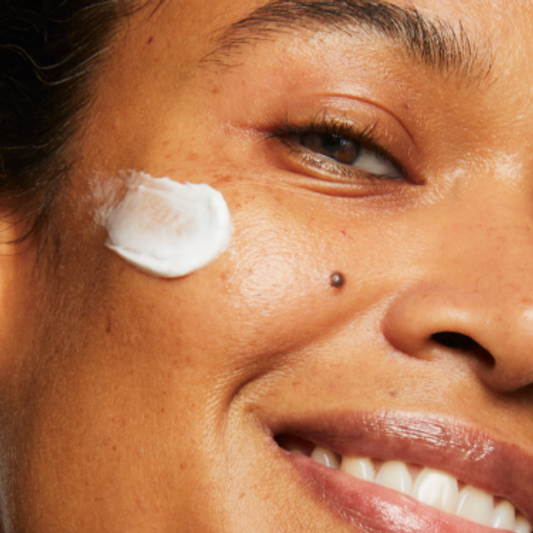 Close-up portrait of a model smiling. They are wearing a swipe of Milk Makeup Vegan Milk Moisturizer on their face.