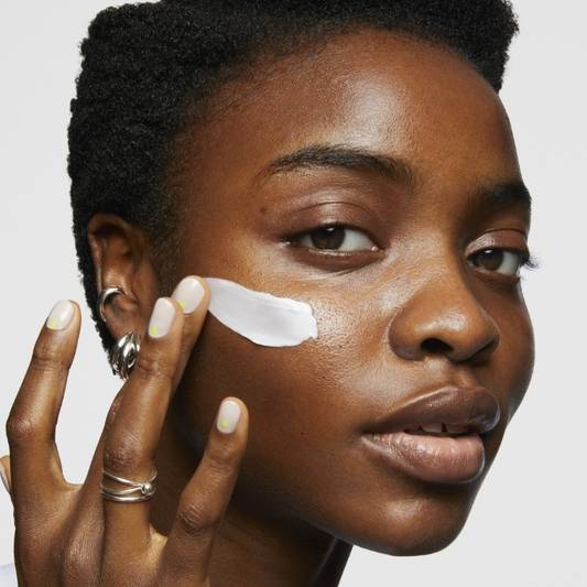 Model applies swipe of Milk Makeup Vegan Milk Moisturizer to her face on a white background