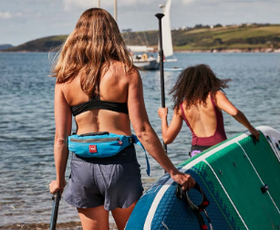 Two people carrying Red Original paddle board wearing personal floatation devices 