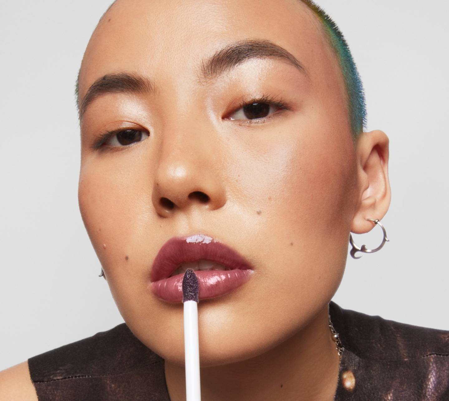 Model applies Milk Makeup Odyssey Lip Oil Gloss in Voyage to lips on a white background.