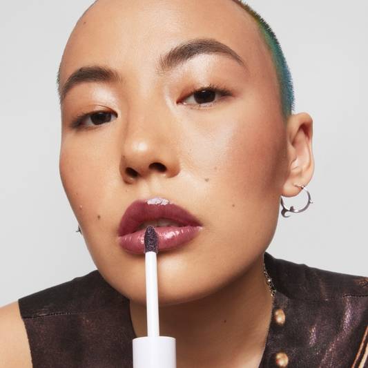 Model applies Milk Makeup Odyssey Lip Oil Gloss in Voyage to lips on a white background.