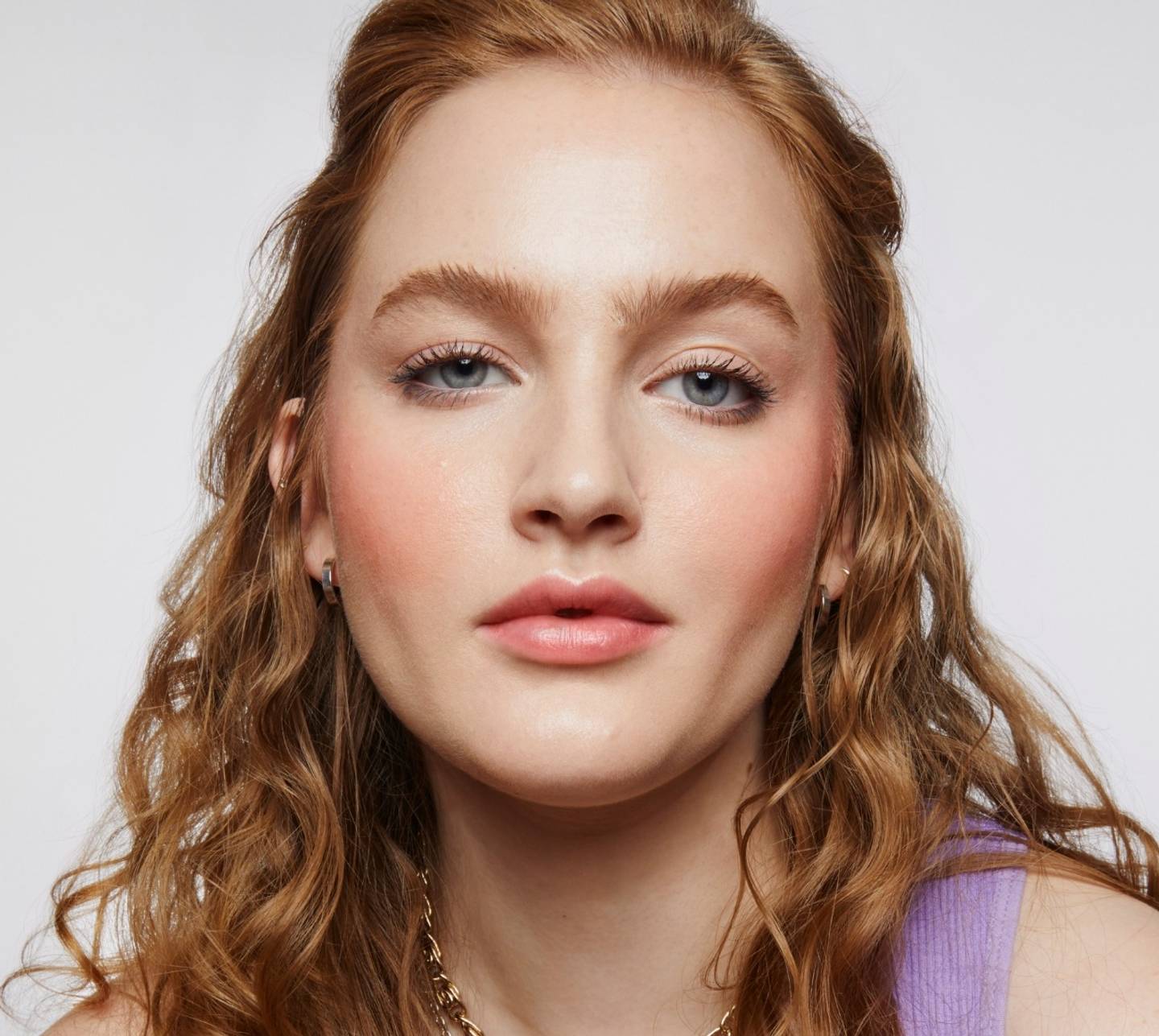Model with wavy strawberry blonde hair wears a full face of Milk Makeup products on a white background