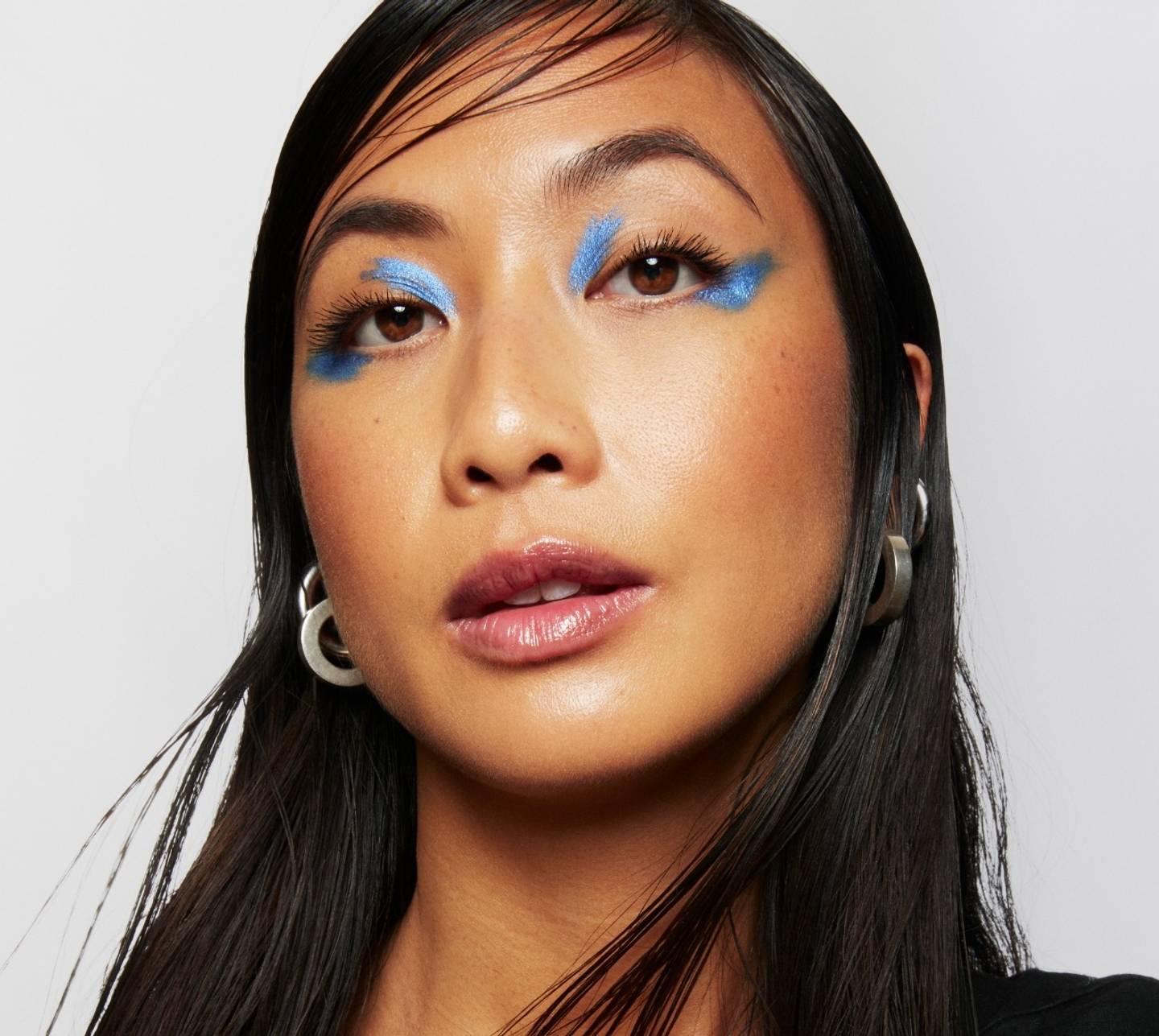 Model wears a full face of Milk Makeup with blue graphic eyeshadow on a white background