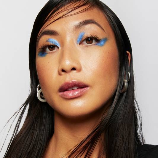 Model wears a full face of Milk Makeup with blue graphic eyeshadow on a white background