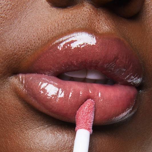 Close-up macro still of a model applying Milk Makeup Odyssey Lip Oil Gloss in Trek.