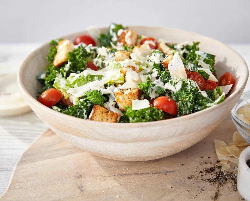 A bowl of kale Caesar salad with homemade croutons prepared using the GreenPan Premiere Titanium Cutlery 12-Piece Knife Block Set with walnut handles. 