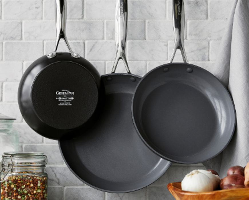 GreenPan Valencia Pro 3-Piece frypan set hanging in front of gray tile kitchen backsplash.