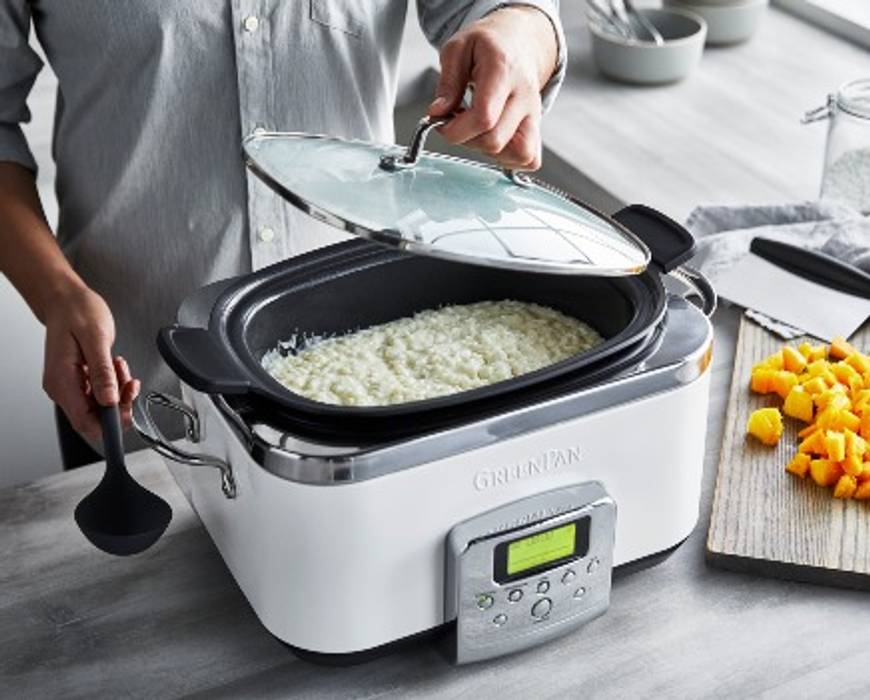 A person standing at a kitchen counter lifting the lid off the GreenPan Elite 6-Quart Slow Cooker while making mango tapioca pudding.