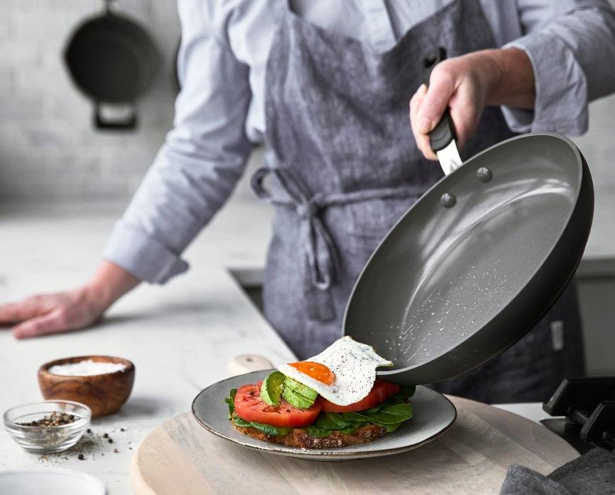 Person sliding an egg off a GreenPan Levels Stackable Ceramic Frypan and onto a plate.