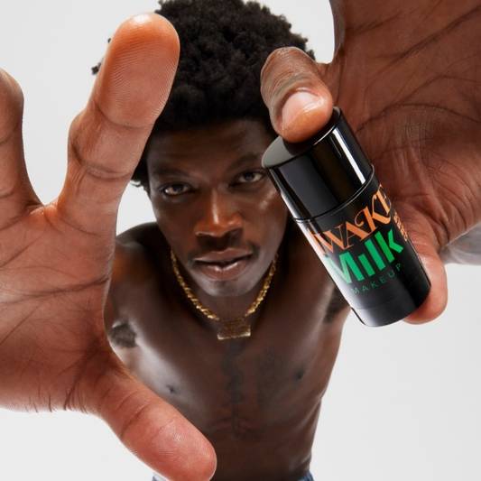 Close-up of model holding stick of Milk Makeup x Awake NY Body Butter on a white background