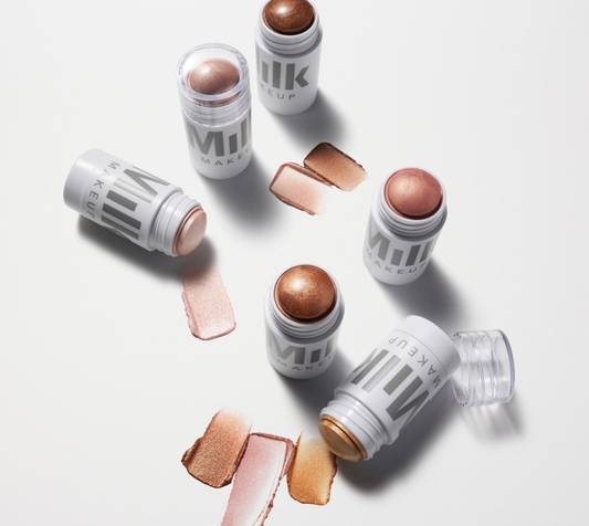 Overhead shot of Milk Makeup Highlighter sticks in shades Spark (golden copper), Flare (rose gold), and Strobe (gold) next to their swatches on a white background.
