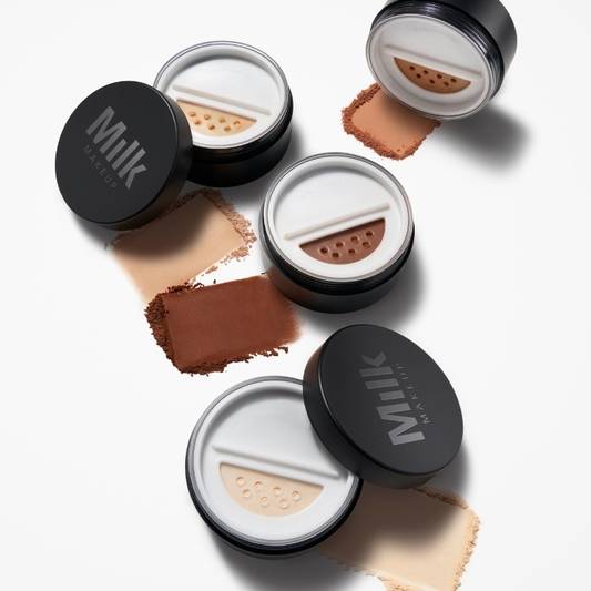 Product shot of four shades of Milk Makeup Pore Eclipse Matte Translucent Setting Powder next to a bit of the powder on a white background