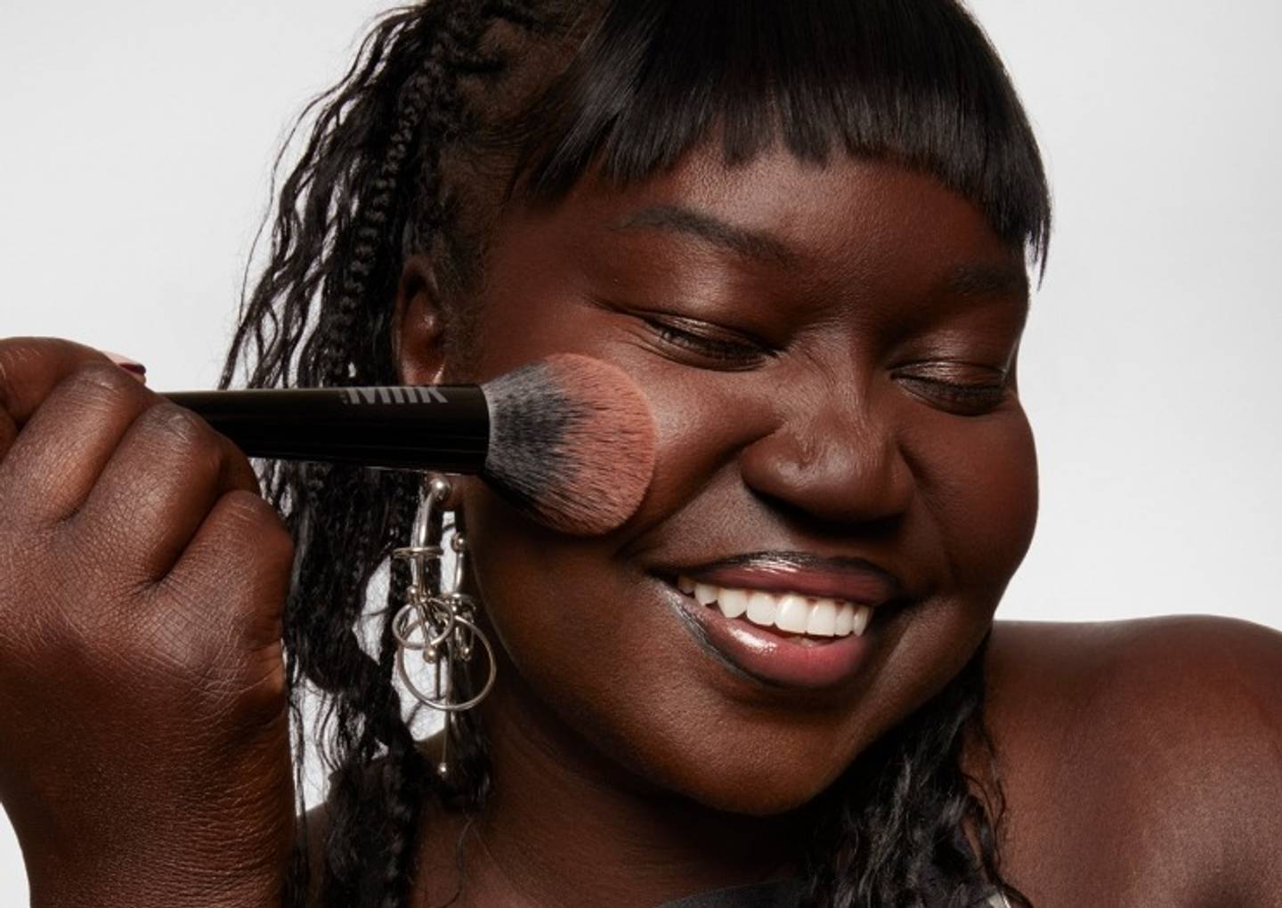 Model applies Milk Makeup Pore Eclipse Matte Translucent Setting Powder with Pore Eclipse Setting Powder Brush on a white background