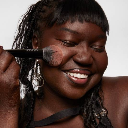 Model applies Milk Makeup Pore Eclipse Matte Translucent Setting Powder with Pore Eclipse Setting Powder Brush on a white background