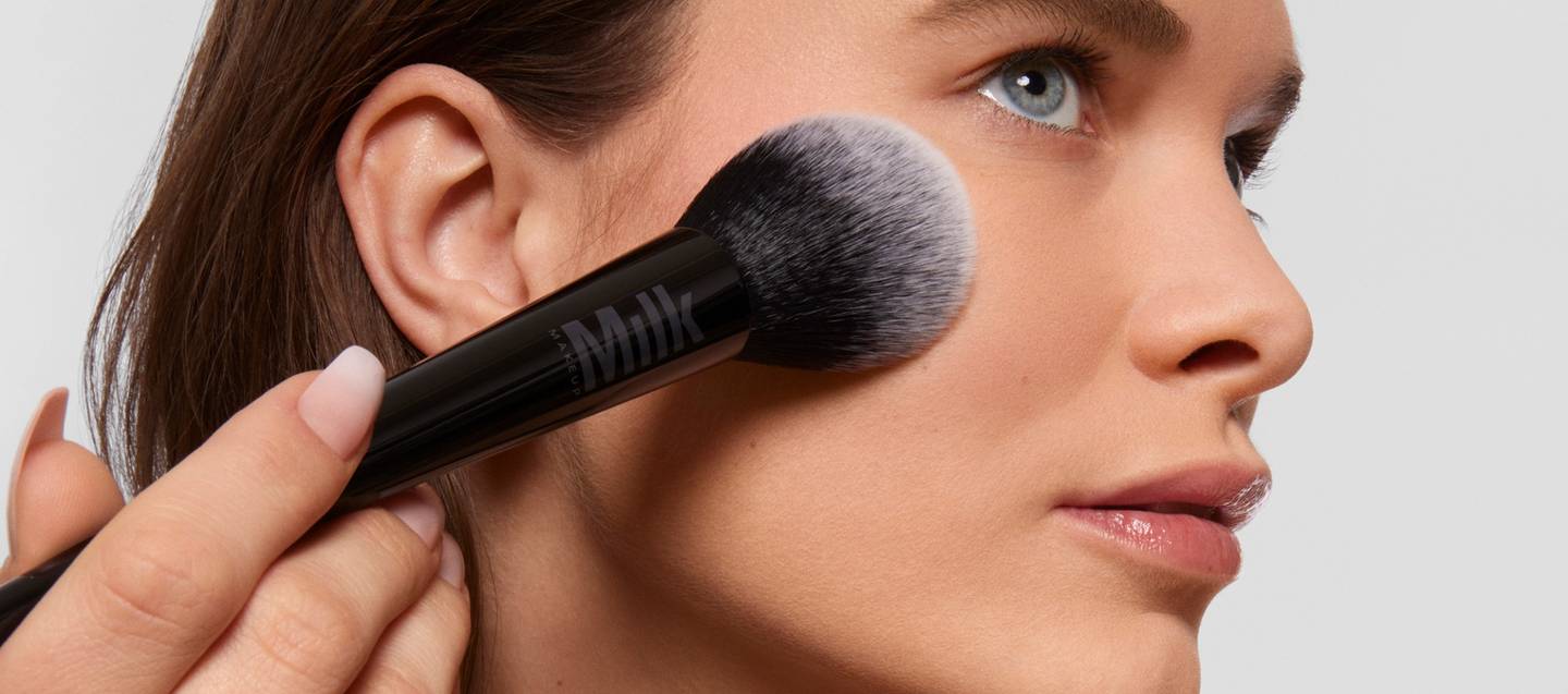 Model applies Milk Makeup Pore Eclipse Matte Translucent Setting Powder to face with the Pore Eclipse Powder Brush against a white background