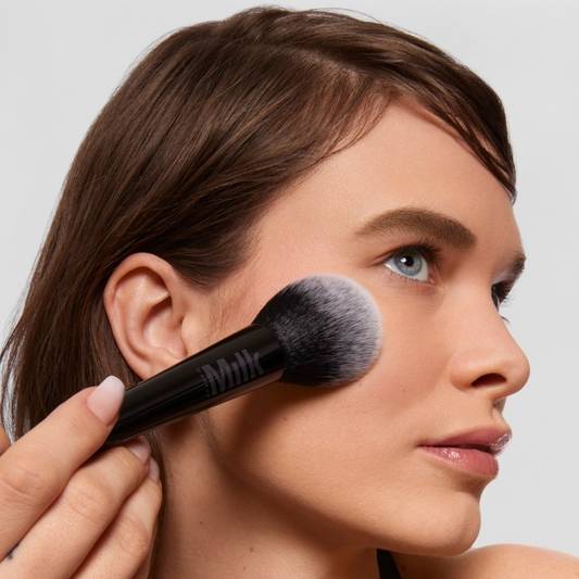 Model applies Milk Makeup Pore Eclipse Matte Translucent Setting Powder to face with the Pore Eclipse Powder Brush against a white background