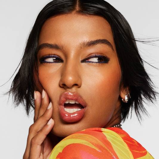 Model wears KUSH Lip Oil in Orange Crush on a white background