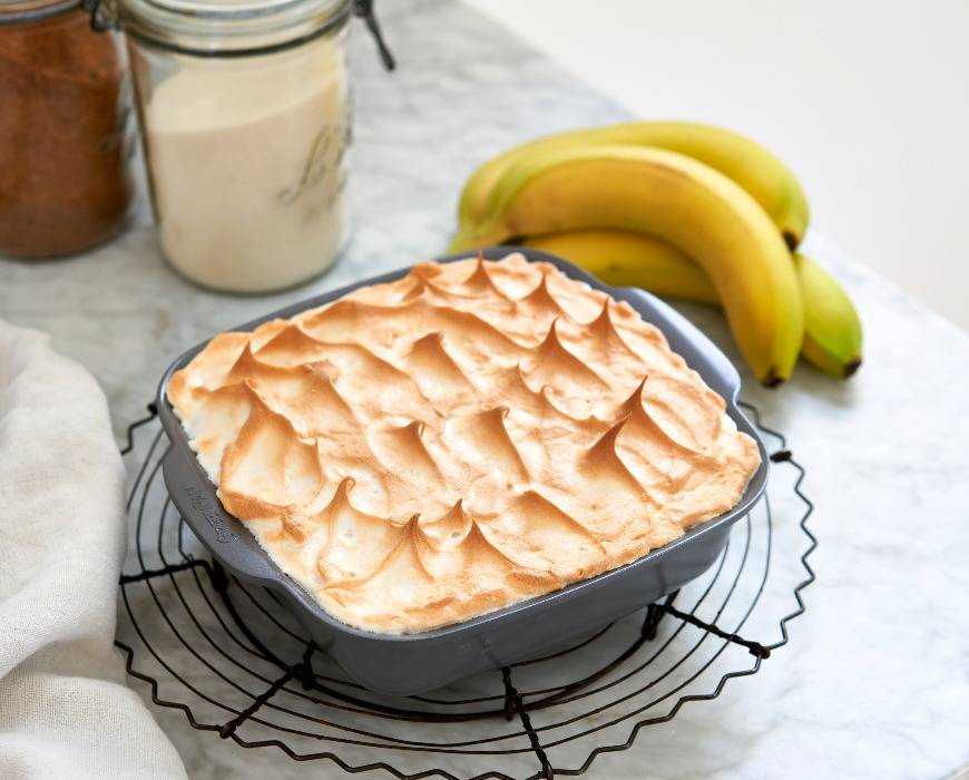 Banana pudding with a torched meringue topping, served in GreenPan ovenware with bananas in the background