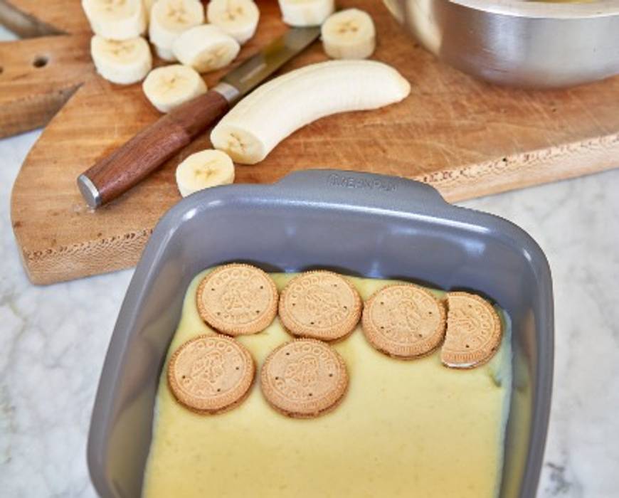 Banana pudding recipe process - Goodie Girl Cookies being layered into GreenPan ovenware; cut bananas in the background