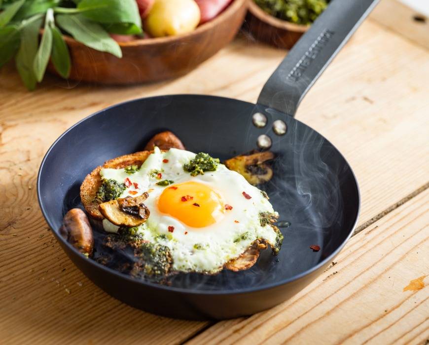 Merten and Storck 8-inch Carbon Steel Skillet on a wooden kitchen counter with a sunny-side up eggs and mushrooms steaming on the pan