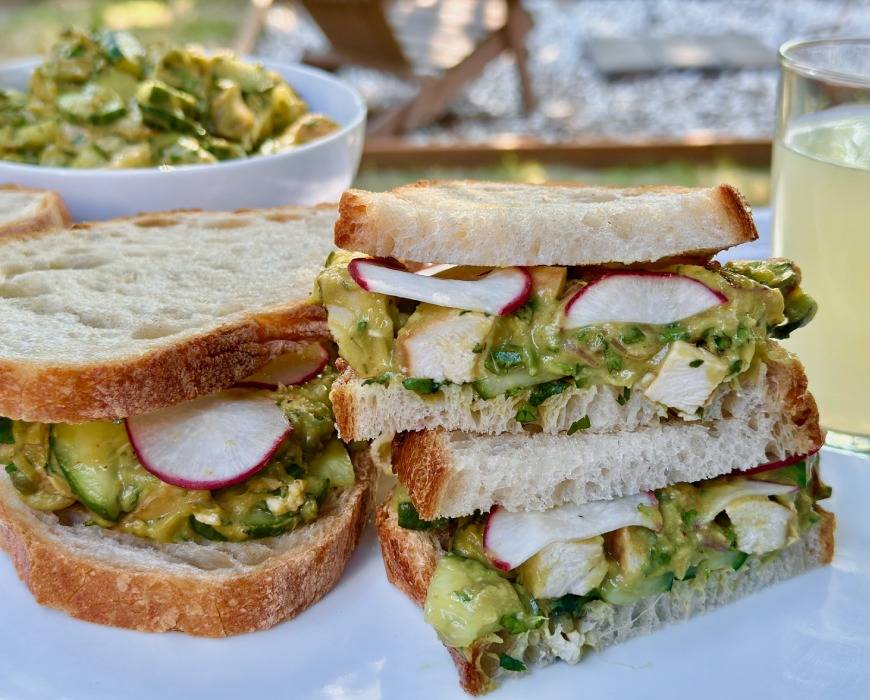 Cross section of Newman's Own avocado salad sandwiches outdoors, with lemonade in the background