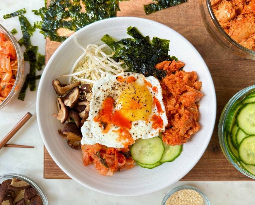 Colorful bowl of bibimbap - a bowl of rice topped with egg, kimchi, mushrooms, seaweed paper, bean sprouts, tinned fish, and more!