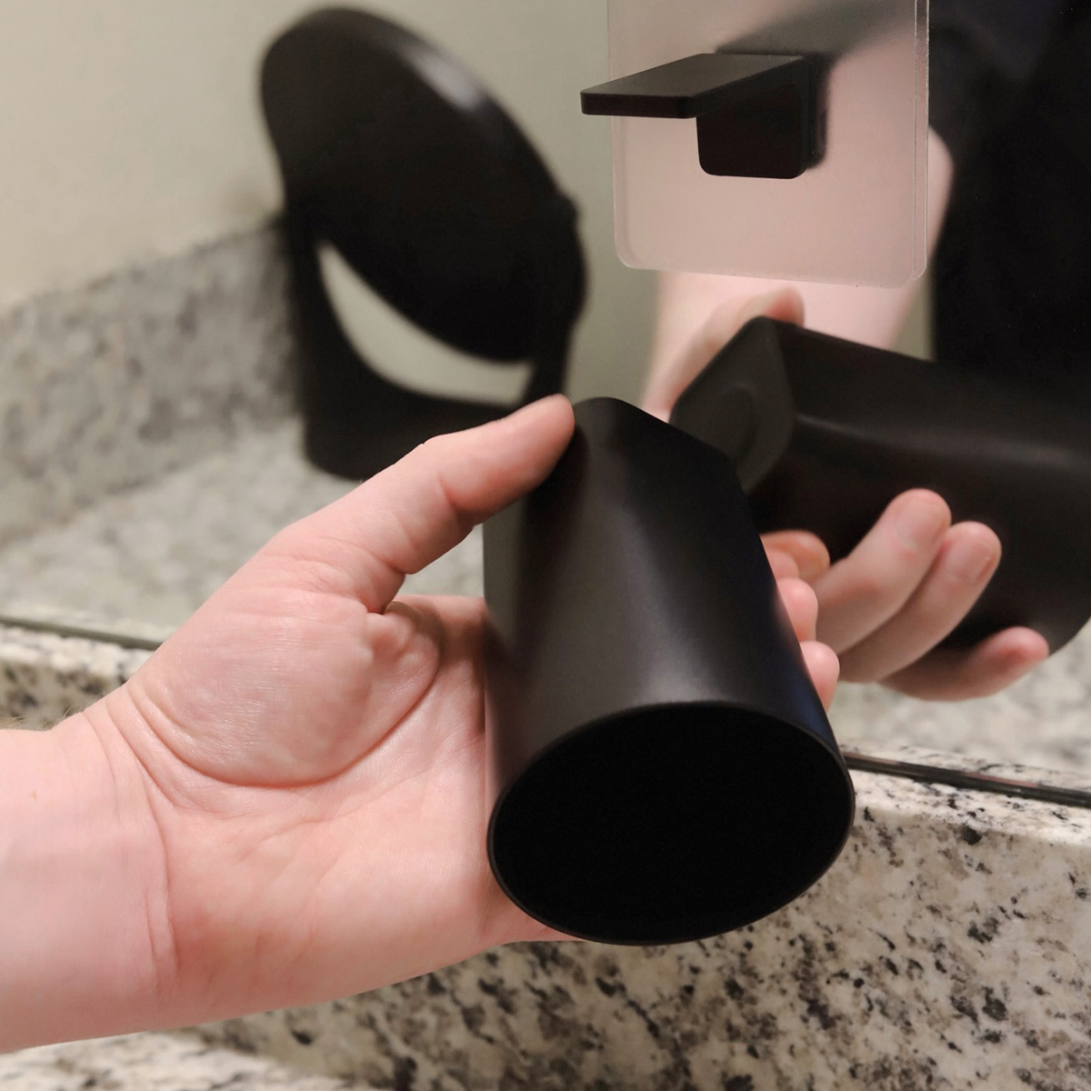 A hand holding the cup of the Traceless Adhesive Magnetic Cup Holder by Yamazaki Home in black.