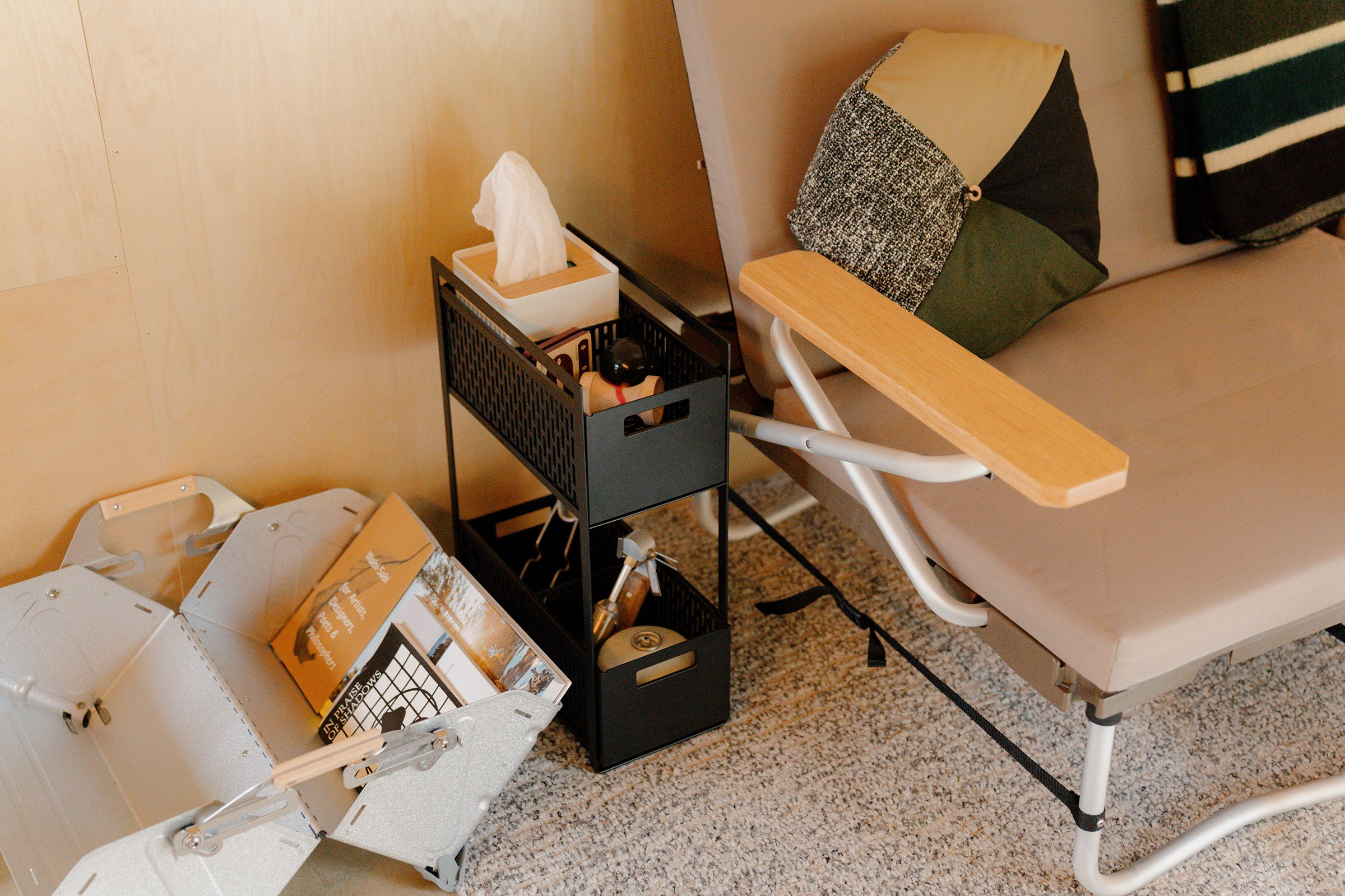 Yamazaki Home Two Tier cabinet storage basket in black holding tissue case next to couch. 