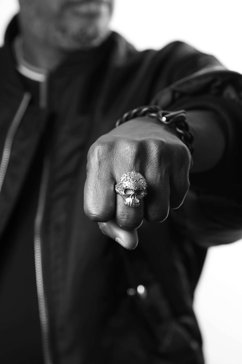 A man's fist wearing a skull ring with an oak leaf pattern on it.