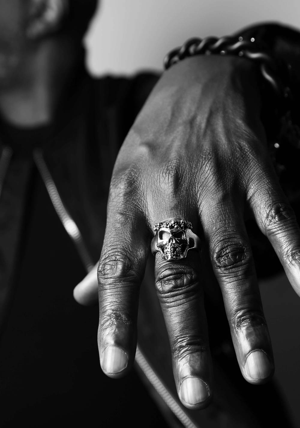 A male's hand wearing a silver skull crowned ring on the middle finger.
