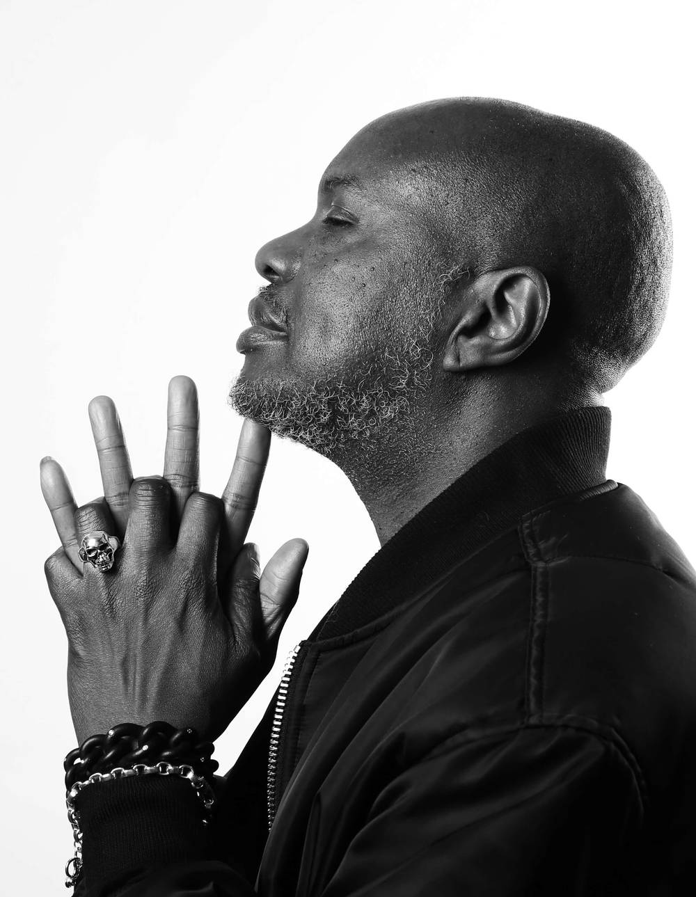 A man with his hands on his chin is wearing a silver full face skull ring.
