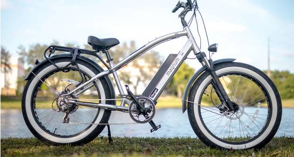 Silver Magnum Ranger e-bike parked on grass with sunny sky and river in blurred backdrop