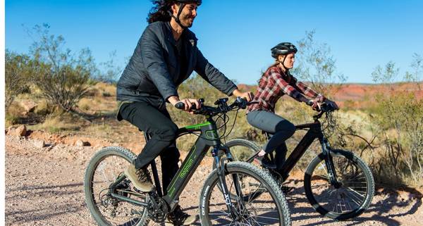 Two riders on Magnum Summit electric bikes on gravel trail with blue sky in the background