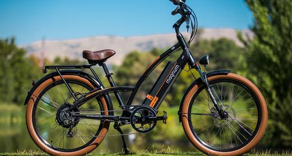 Black and orange Magnum Low Rider parked in front of a blurry green backdrop with desert hill and blue sky in the distance