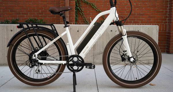 White Magnum Metro 750 electric bike parked on sidewalk in front of brick wall with green ivy
