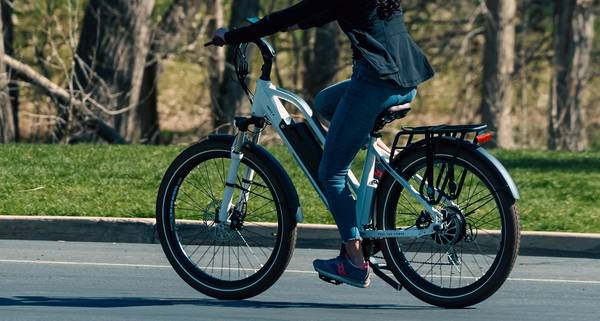 Rider in black jacket and jeans with gray and pink sneakers riding white Magnum Metro X in the street in front of grassy field