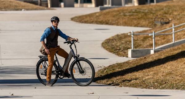 Rider in gray helmet blue shirt vet and khakis pausing on a Magnum Cosmo+ electric bike on wide concrete plaza