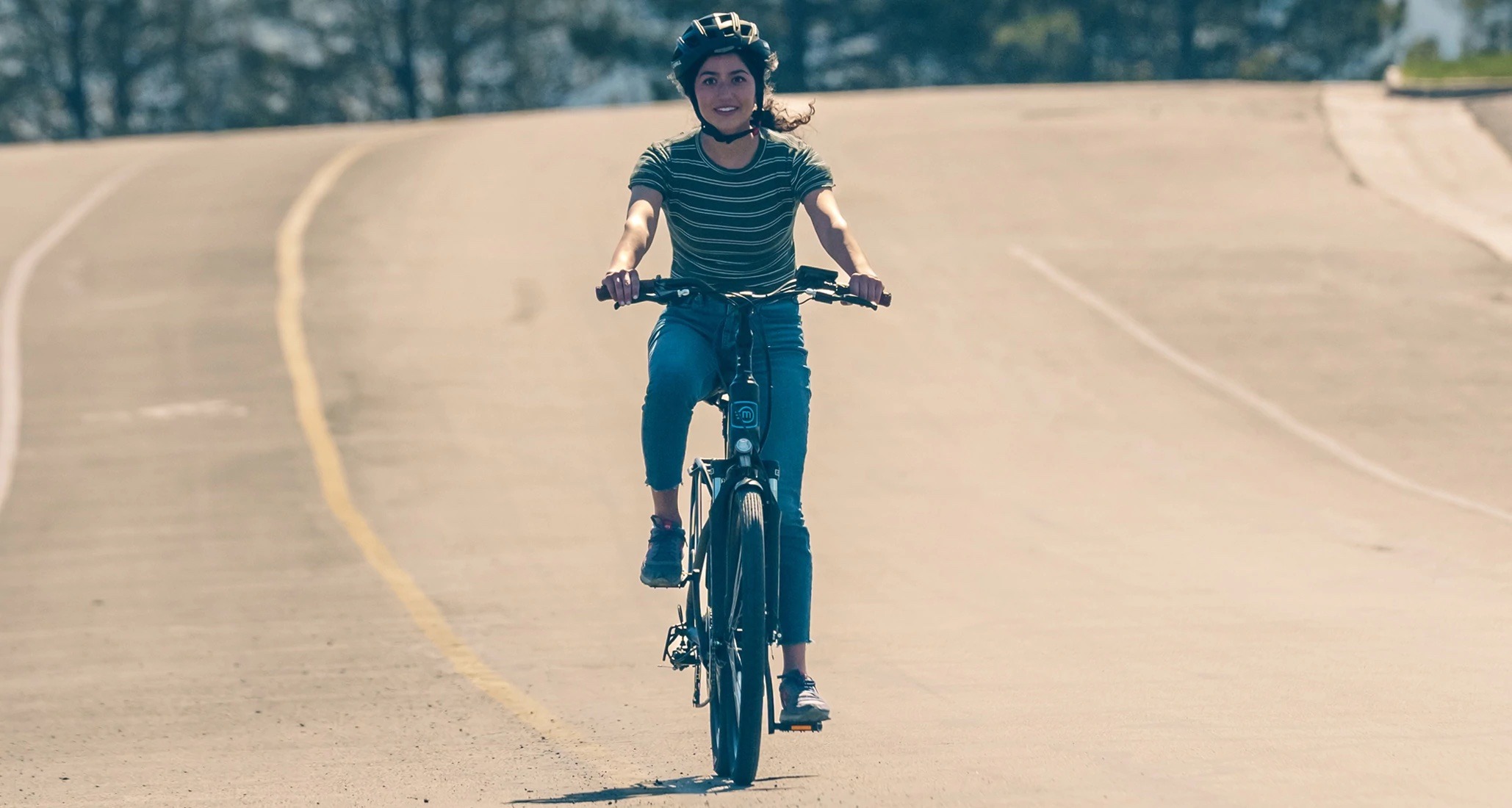 Rider in black helmet striped shirt and jeans riding a Magnum Navigator S electric bike on an empty downhill street