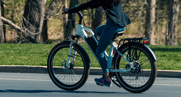 Rider from the shoulders down on a Magnum Metro X touring e-bike riding on the street with grass and trees on the sidewalk