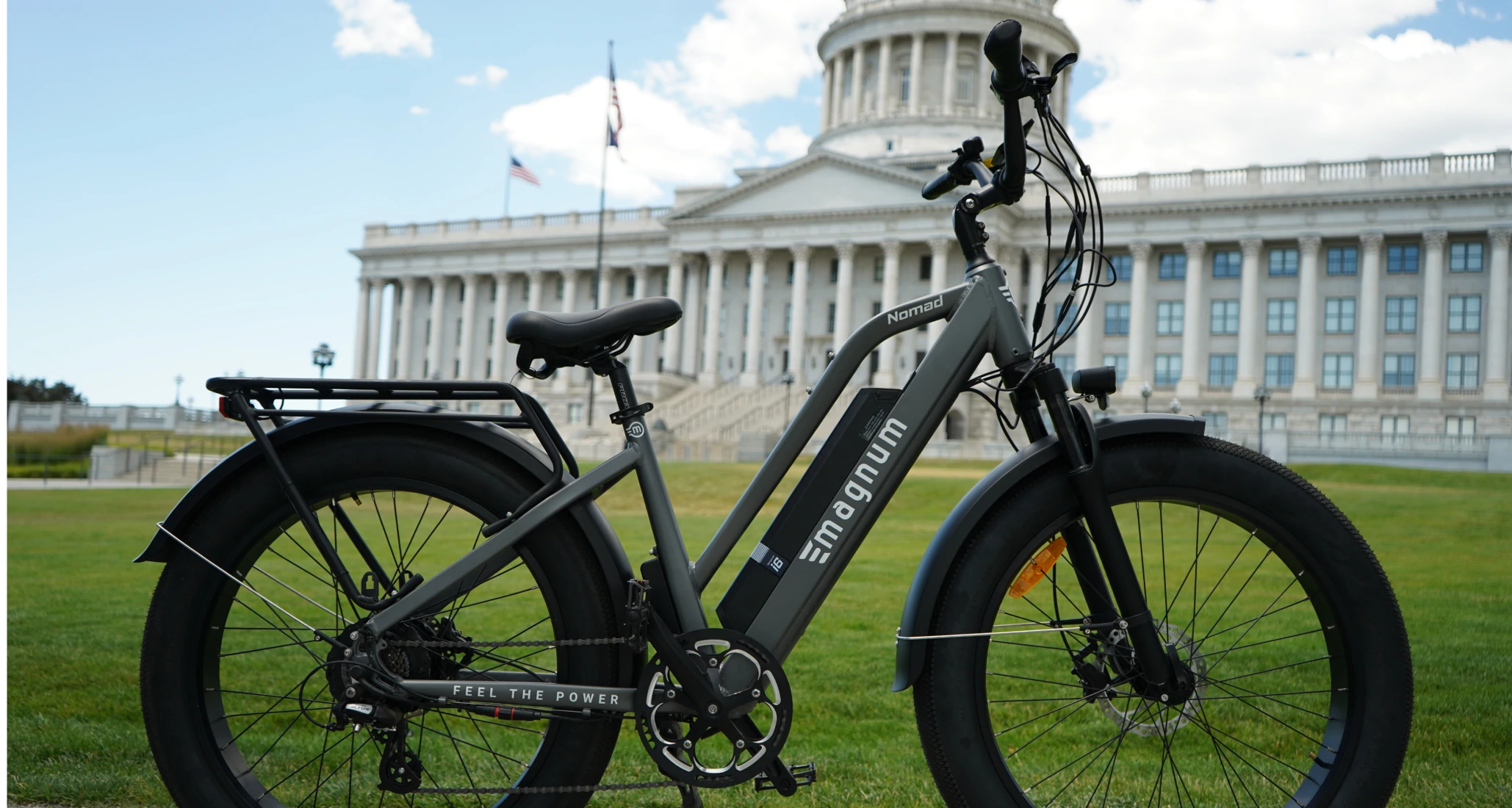 Close-up of a Gray Magnum Nomad e-bike on a green lawn in front of a government building