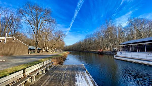 The Erie Canal as seen from Erie Canal Park in Camillus, NY along the Erie Canalway e-bike path, featuring a dock with seating, bright blue skies and bare trees on a clear winter day